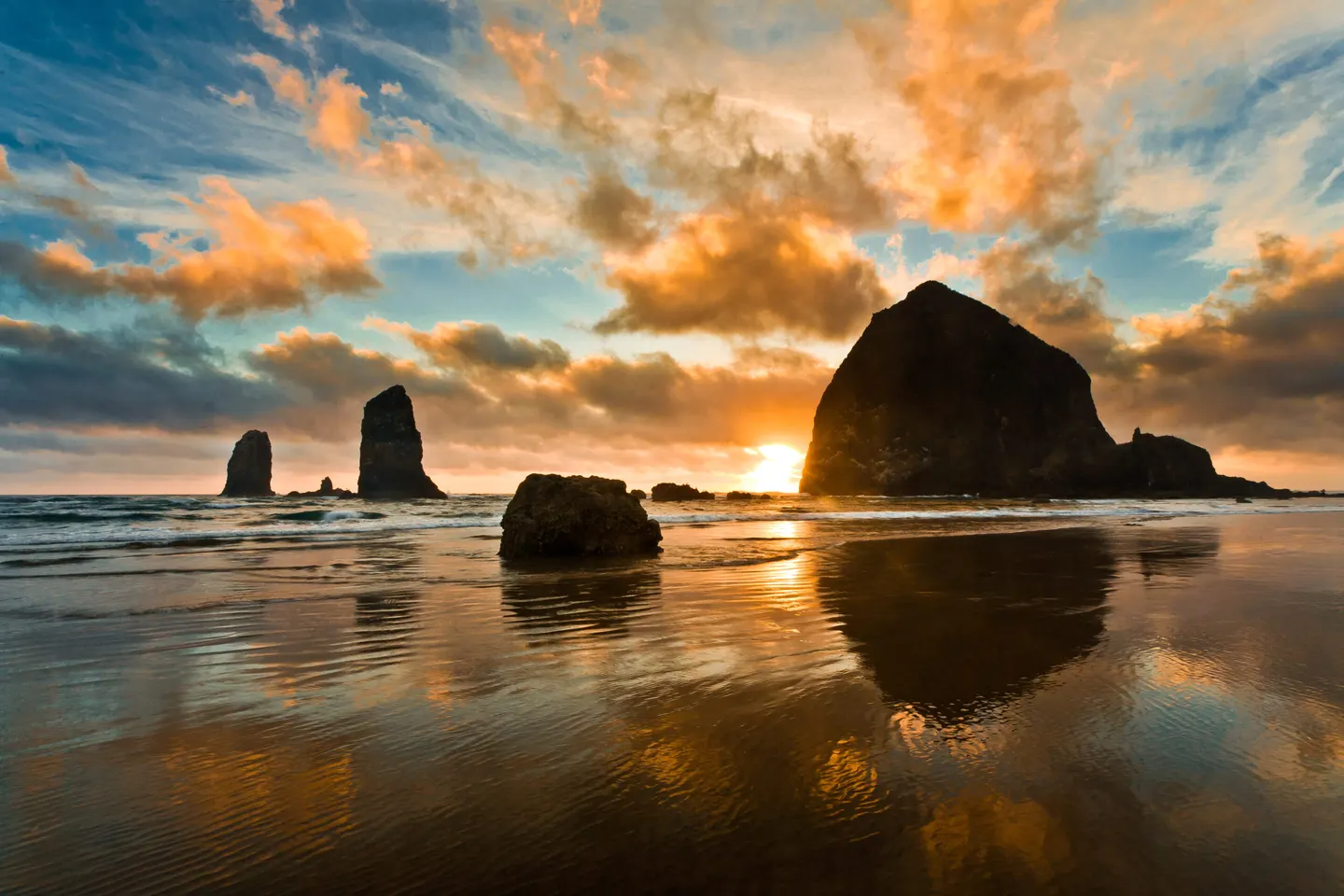 Haystack Rock and the Needles at Cannon Beach at sunset, reflected in the wet sand